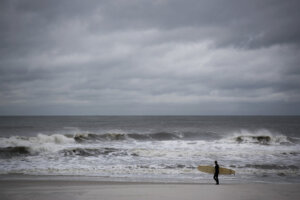 Male surfer strolling along Long Beach, New York, USA